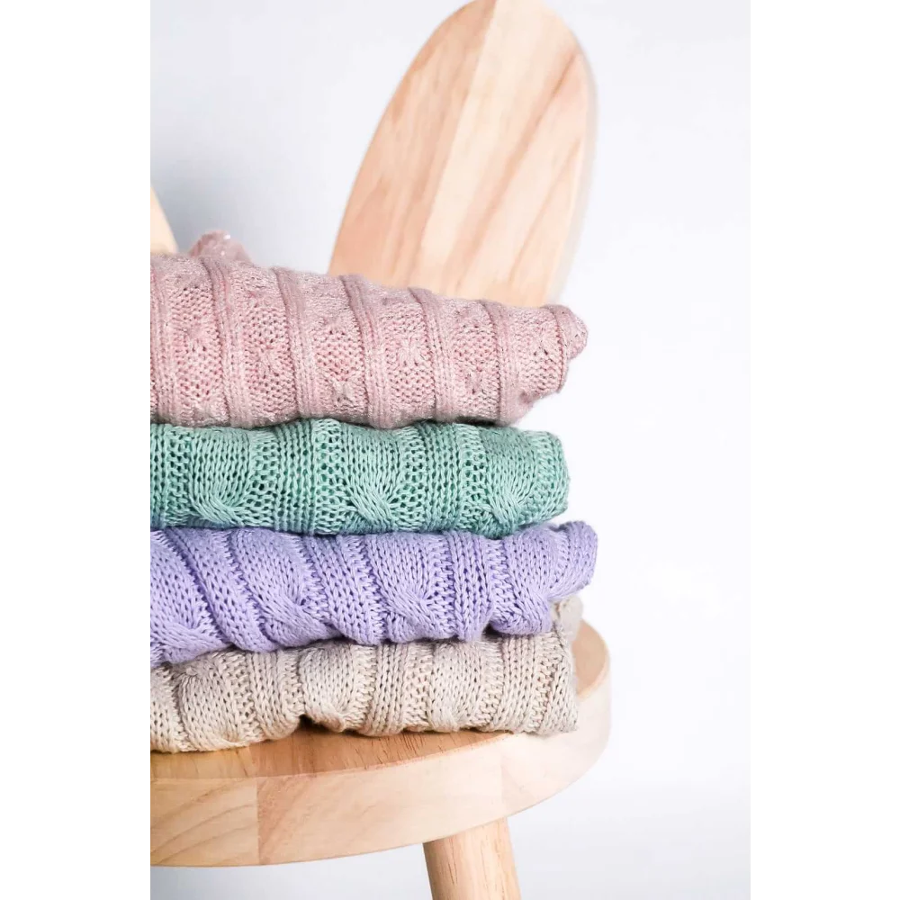 Stack of cream pastel-colored knitted wool sweaters with cable patterns for pet fashion etoile dla psa on wooden stool
