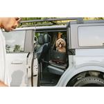 Czarno-brązowy transporter dla psa o solidnej, wyściełanej konstrukcji bezpiecznie stoi na tylnym siedzeniu SUV-a.