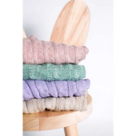 Stack of pastel-colored knitted wool sweaters with cable patterns on a wooden stool for pet fashion etoile chroni szyję pupila